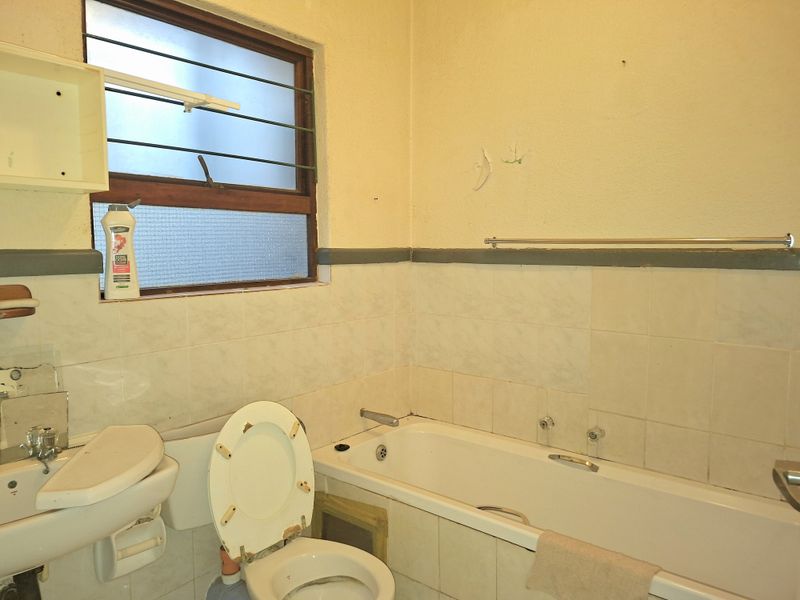 A dated bathroom featuring a standard bathtub, pedestal basin, and toilet, requiring renovation and modernization of fixtures and finishes.