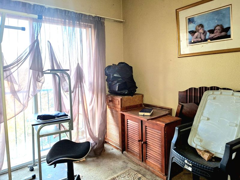 A bedroom featuring a sliding glass door with balcony access, currently requiring significant cosmetic updates and refurbishment to improve its overall condition.