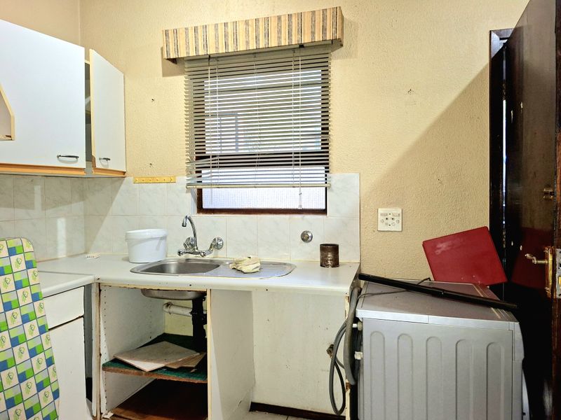 A dated kitchen area featuring a stainless steel sink, tiled splashback, and built-in cabinetry in need of renovation and repair.