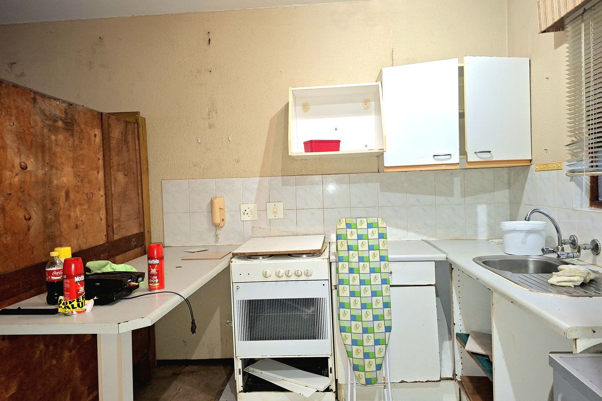 A dated kitchen featuring a freestanding stove, stainless steel sink, and basic cabinetry, currently in need of significant renovation and cosmetic updates.