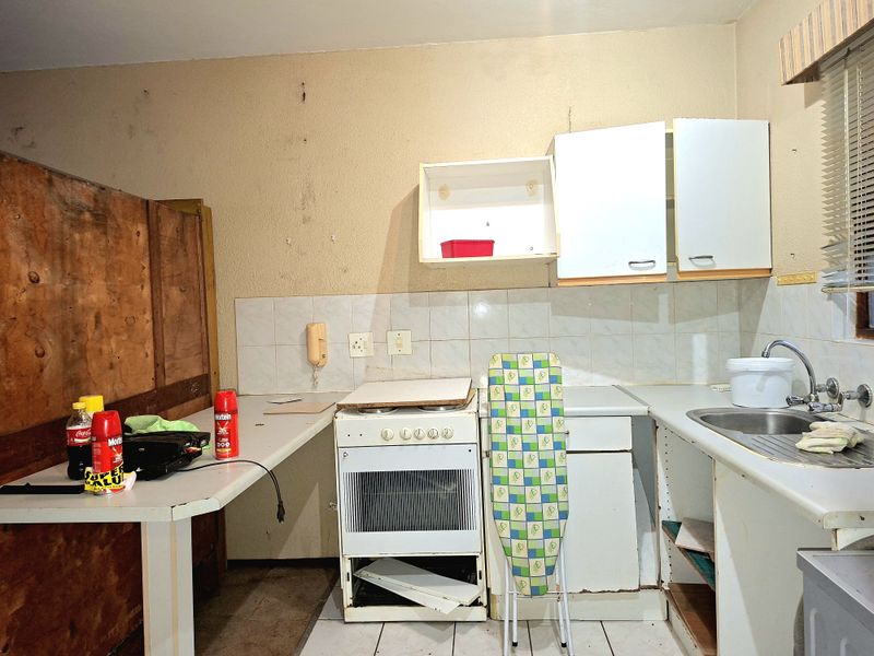 A dated kitchen featuring a freestanding stove, stainless steel sink, and basic cabinetry, currently in need of significant renovation and cosmetic updates.