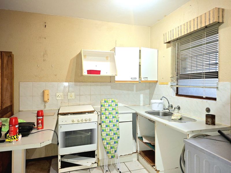 A dated kitchen featuring basic cabinetry, a stainless steel sink, and a freestanding stove, requiring significant renovation and modernization of fixed finishes.