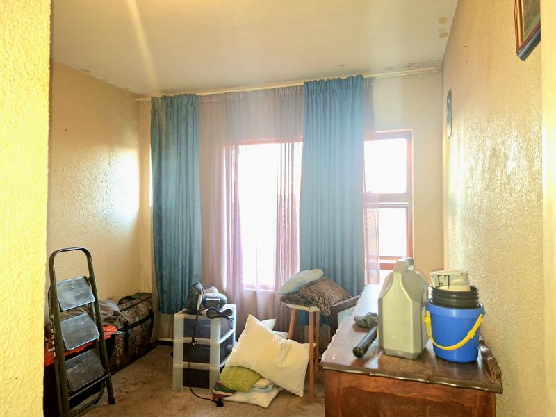 A bedroom space featuring a window with curtain rails, requiring cosmetic updates to the walls and flooring to improve its overall condition.