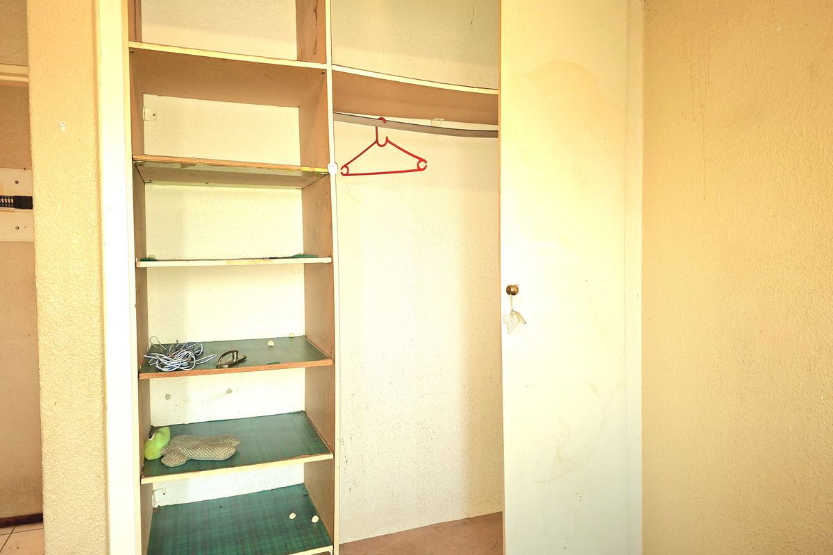 A bedroom featuring a built-in wardrobe with open shelving, showing signs of wear and requiring cosmetic updates.