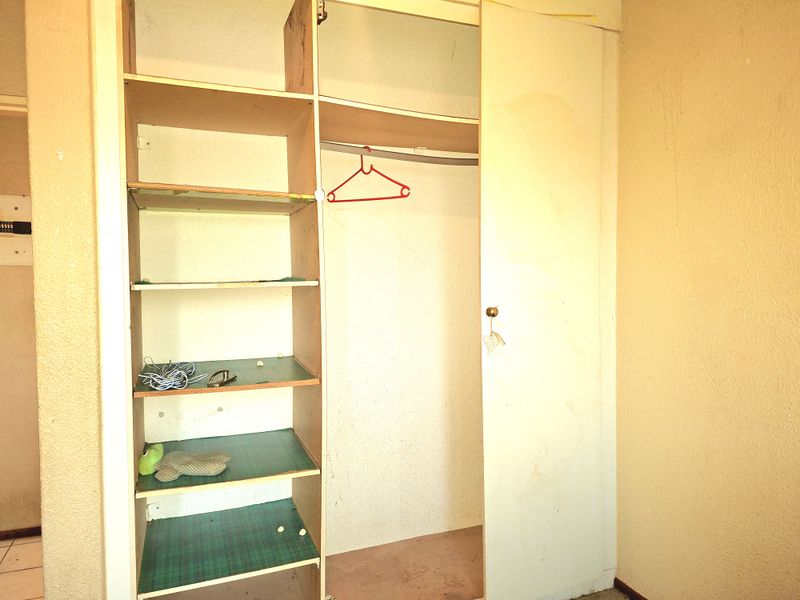 A bedroom featuring a built-in wardrobe with open shelving, showing signs of wear and requiring cosmetic updates.