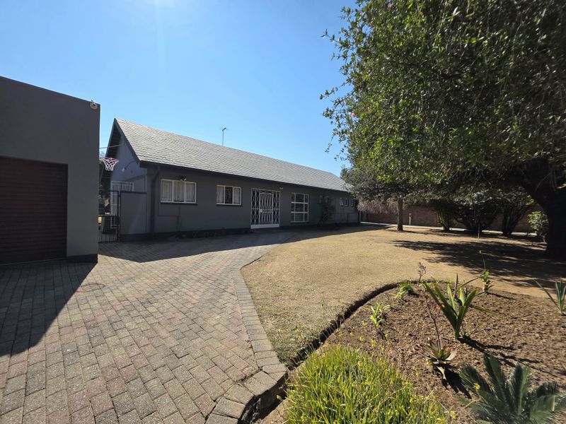 Front view of the property featuring a paved driveway, well-maintained garden, and a secure entrance with a tiled roof structure.