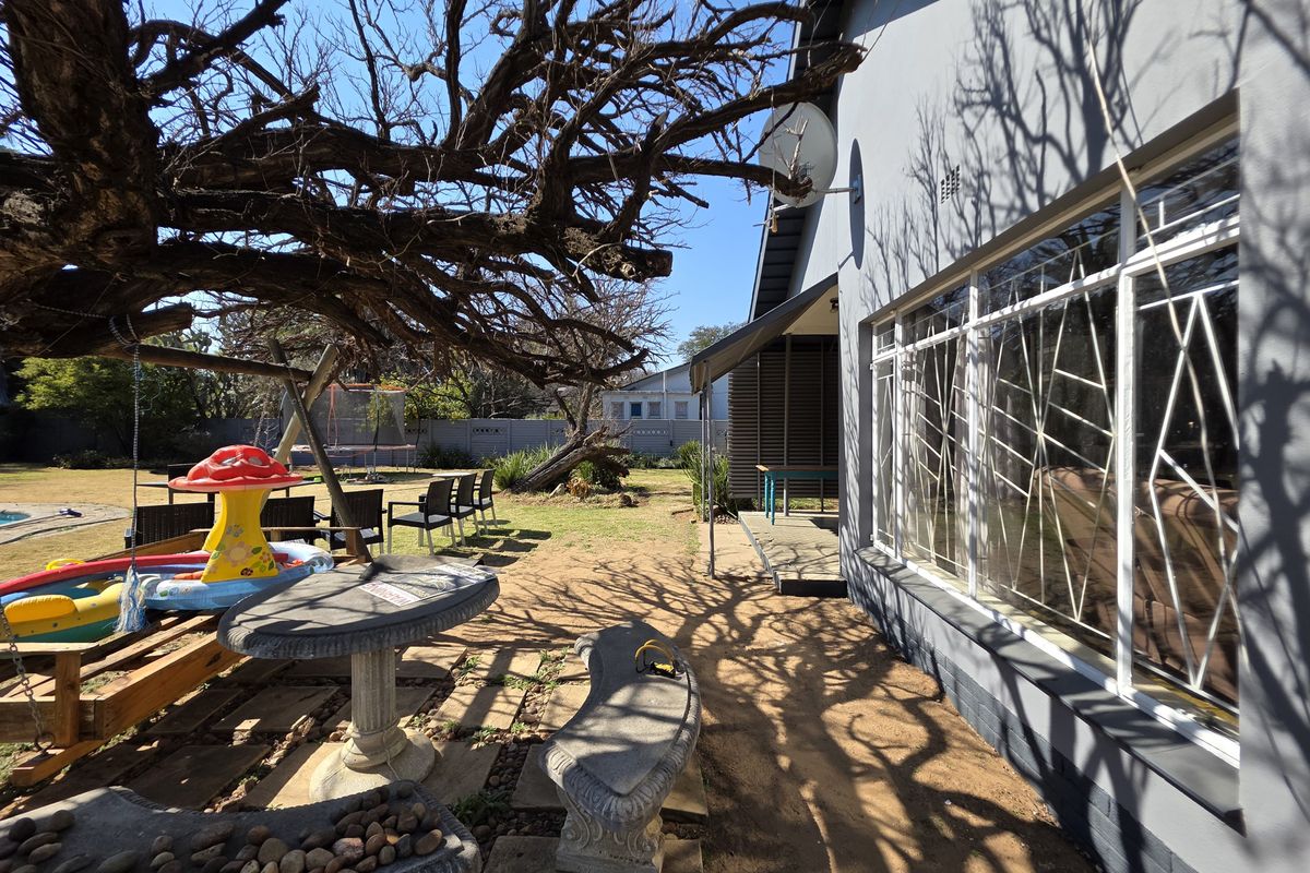 Rear exterior view of the property featuring a paved patio area, security bars on windows, and a large garden space.