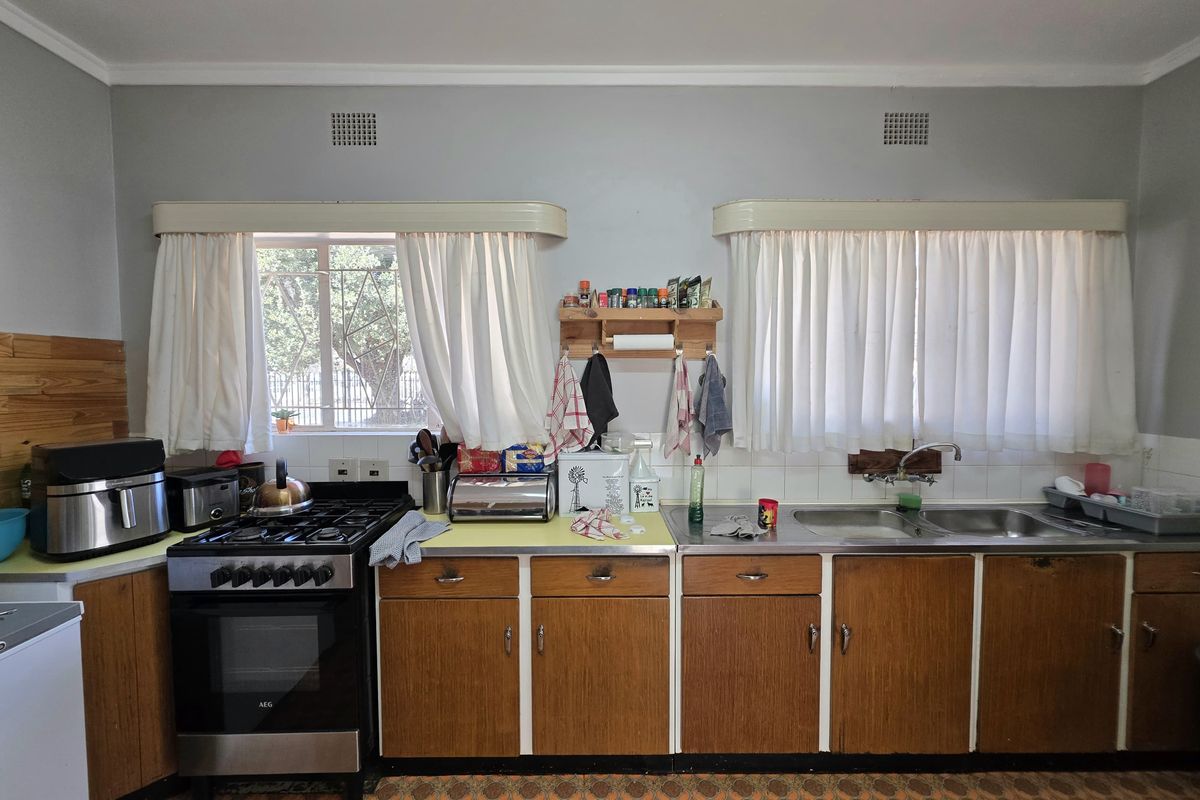 A dated kitchen featuring wooden cabinetry, laminate countertops, a gas stove, and a double basin sink with tiled splashbacks.