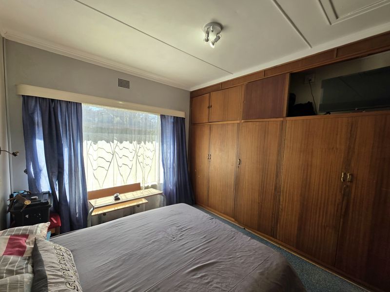 A bedroom featuring extensive built-in wooden cabinetry and a large window, offering functional storage space with potential for cosmetic updates.