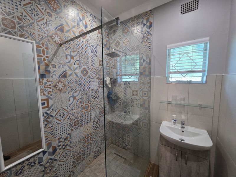 Modern bathroom featuring a walk-in shower with a rain shower head, decorative patterned wall tiles, and a vanity basin with storage cabinet.
