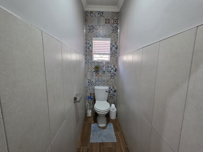 A compact guest bathroom featuring patterned accent tiling, neutral wall tiles, and wood-look floor tiles.