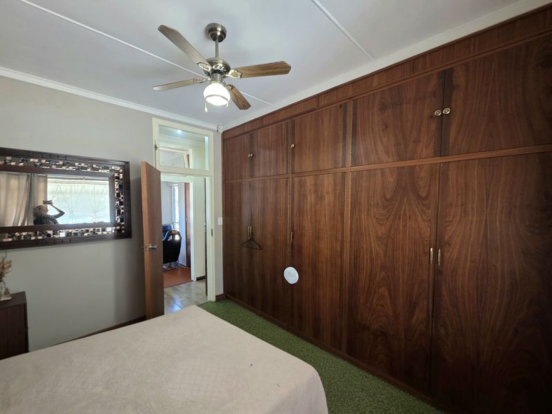A bedroom featuring extensive floor-to-ceiling built-in wooden cabinetry, a ceiling fan, and carpeted flooring.