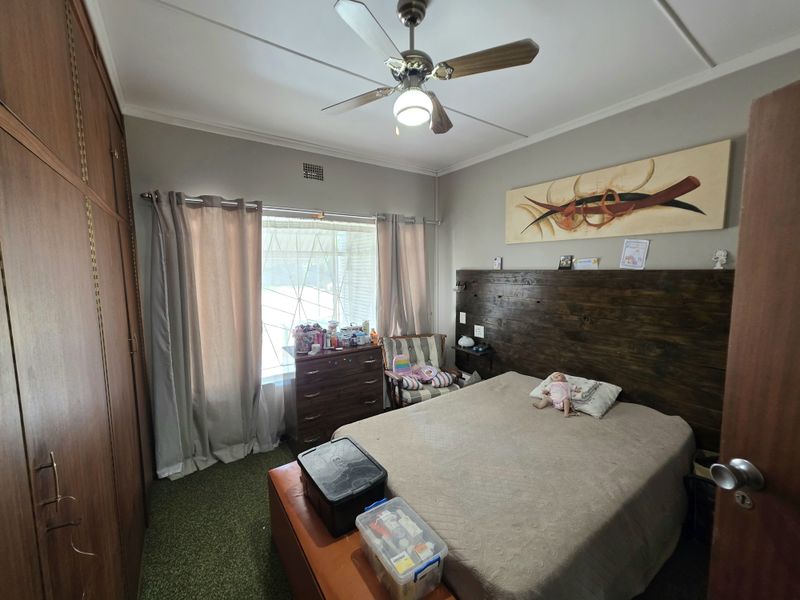 A bedroom featuring built-in wooden cupboards, a ceiling fan, and a custom timber headboard, offering a functional space with classic finishes.