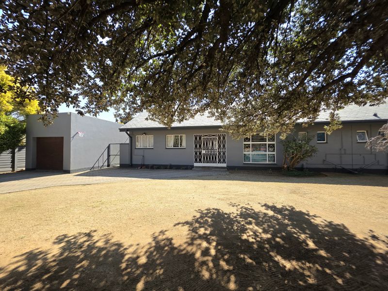 Front view of a single-story house featuring a paved driveway, attached garage, and secure entrance gate, set on a spacious residential lot.