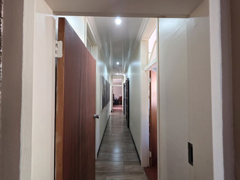 A well-lit hallway featuring modern timber-look floor tiles, recessed downlighting, and clean, neutral wall finishes connecting various rooms.