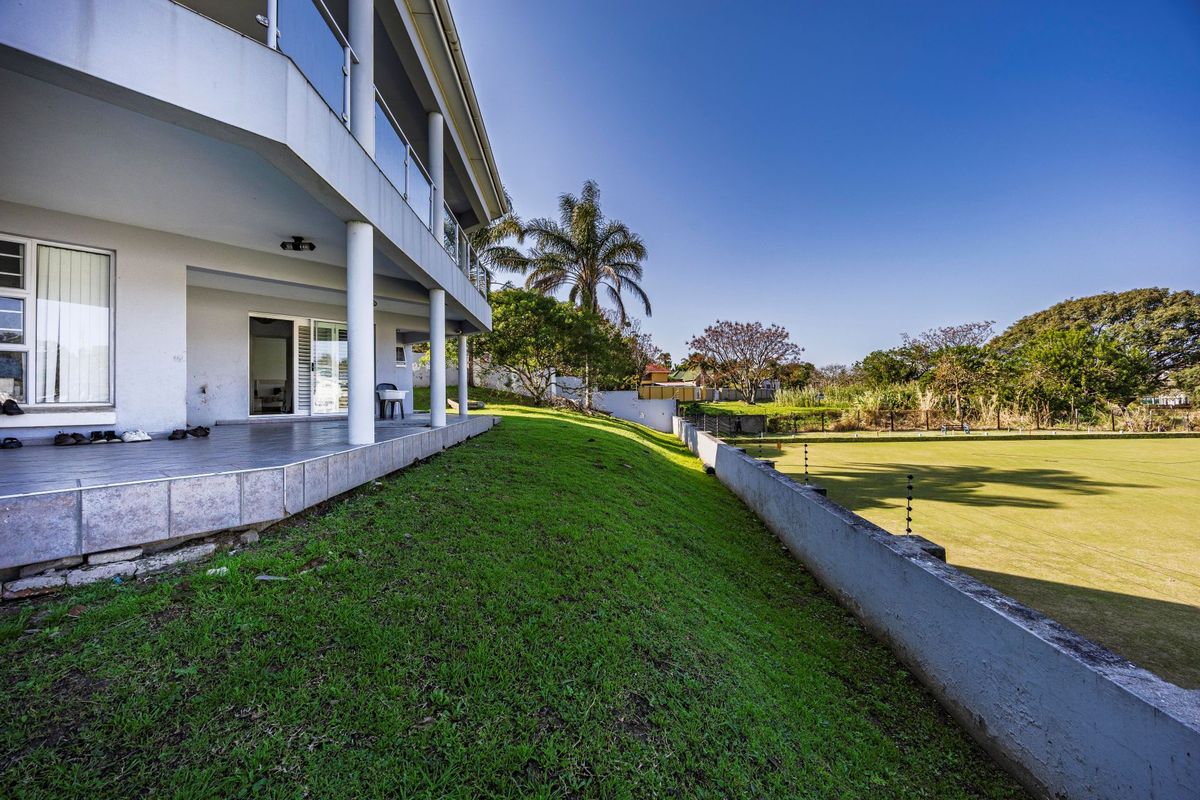 Rear view of the property featuring a covered tiled patio with glass balustrades, overlooking a landscaped garden and retaining wall with electric fencing.