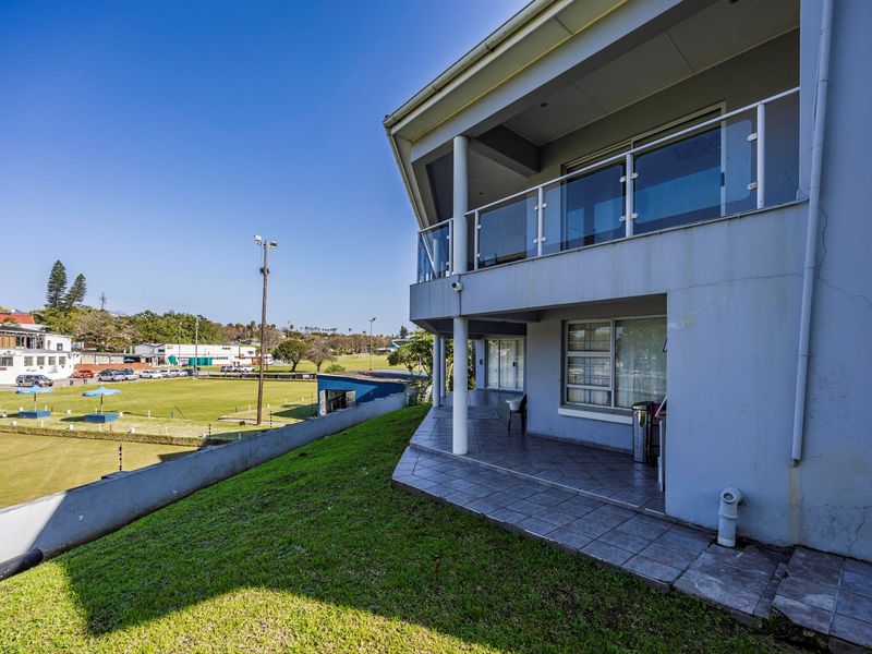 Rear view of the property featuring a tiled ground-level patio, an upper-level balcony with glass balustrades, and views over the adjacent sports field.