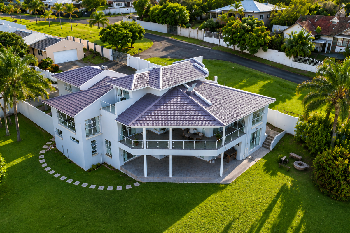 Aerial view of a modern multi-level residential property featuring a tiled roof, expansive wrap-around balcony with glass balustrades, and a well-maintained garden.