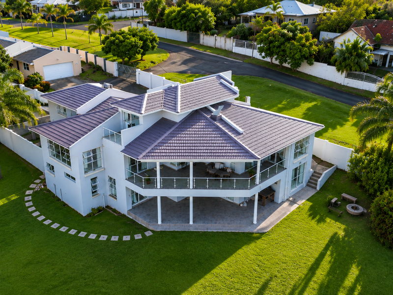 Aerial view of a modern multi-level residential property featuring a tiled roof, expansive wrap-around balcony with glass balustrades, and a well-maintained garden.