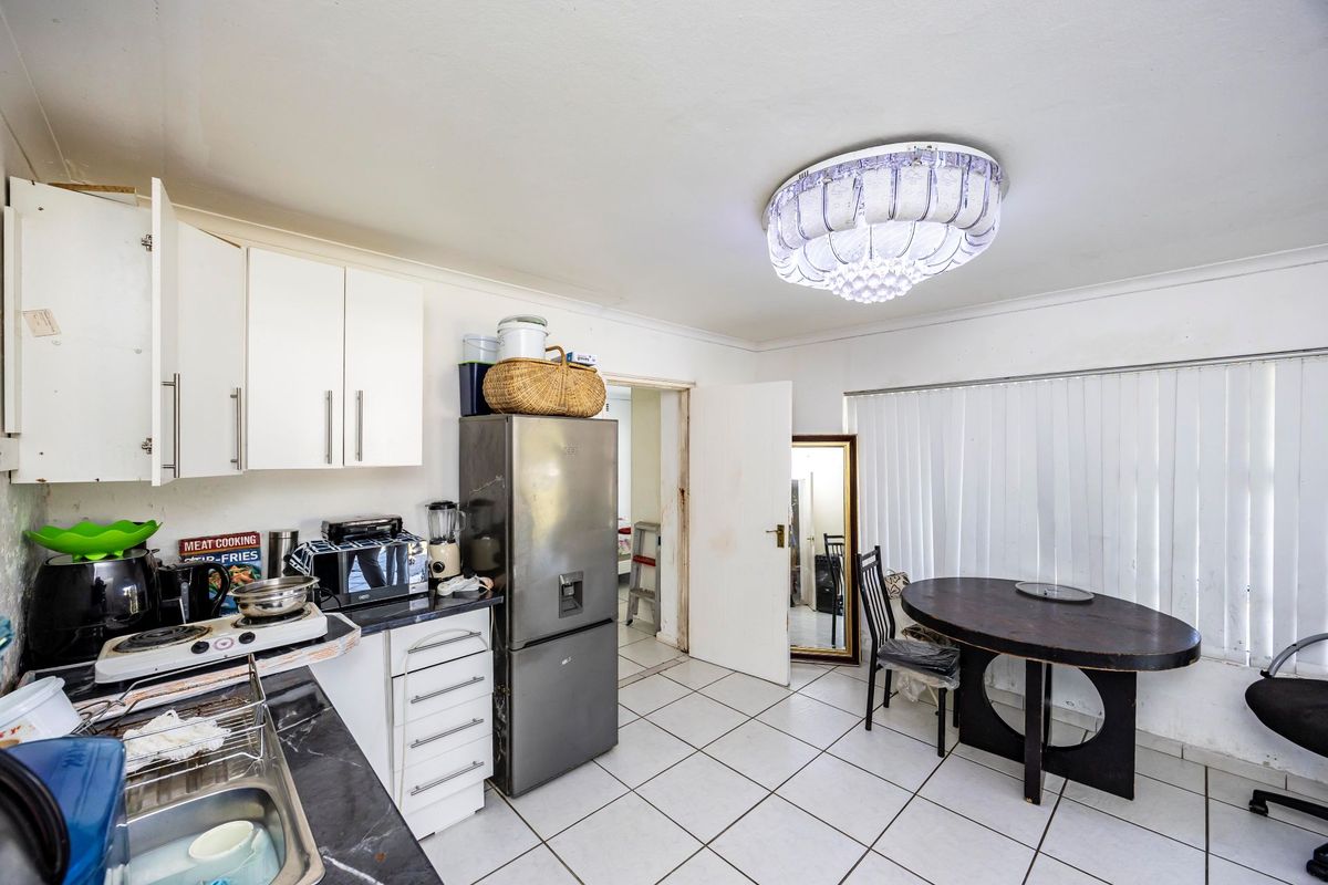 A functional kitchen area featuring white cabinetry, dark countertops, and tiled flooring, offering potential for modernization and aesthetic updates.