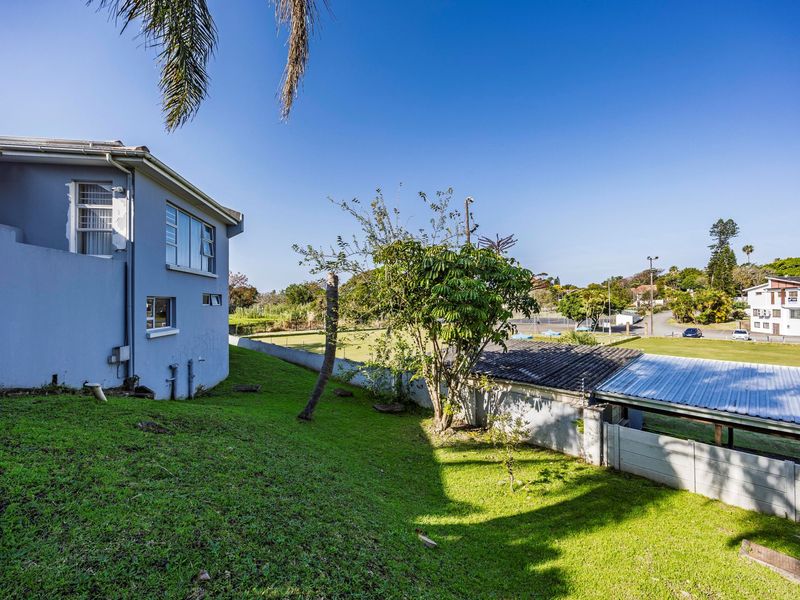 Rear view of the property showing a sloped garden, precast boundary wall, and adjacent outbuilding with a corrugated metal roof.
