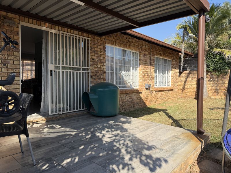 A covered patio area featuring tiled flooring, brick exterior walls, and a metal roof structure, providing a functional outdoor space for the townhouse.