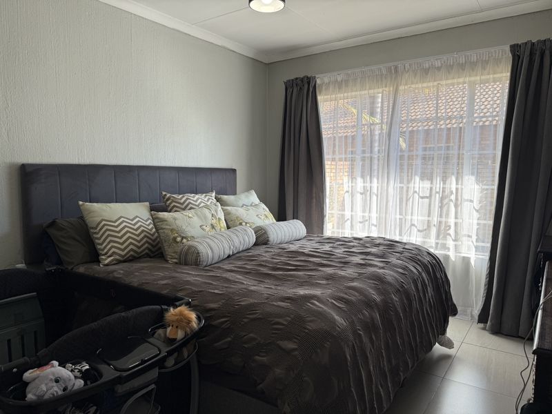 A well-lit bedroom featuring tiled flooring and large windows with curtain tracks, providing a comfortable and functional living space.