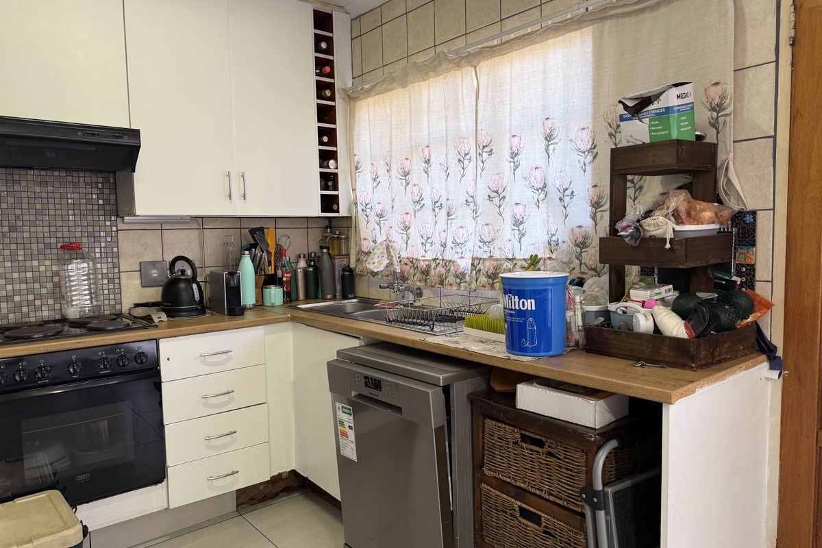 A functional kitchen featuring built-in cabinetry, a hob, oven, extractor fan, and tiled backsplash, requiring some maintenance and cosmetic updates.