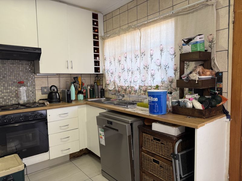 A functional kitchen featuring built-in cabinetry, a hob, oven, extractor fan, and tiled backsplash, requiring some maintenance and cosmetic updates.