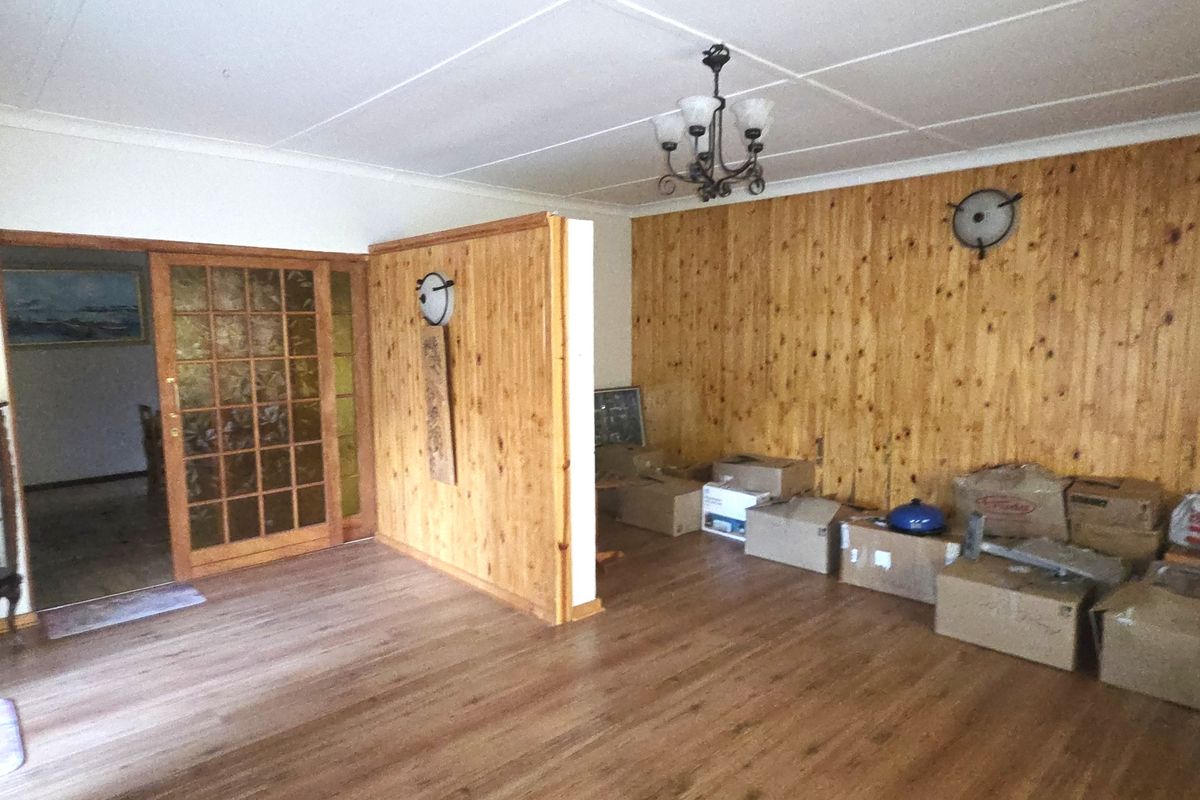 Spacious living area featuring timber wall paneling, laminate flooring, and a sliding glass door leading to an adjacent room.