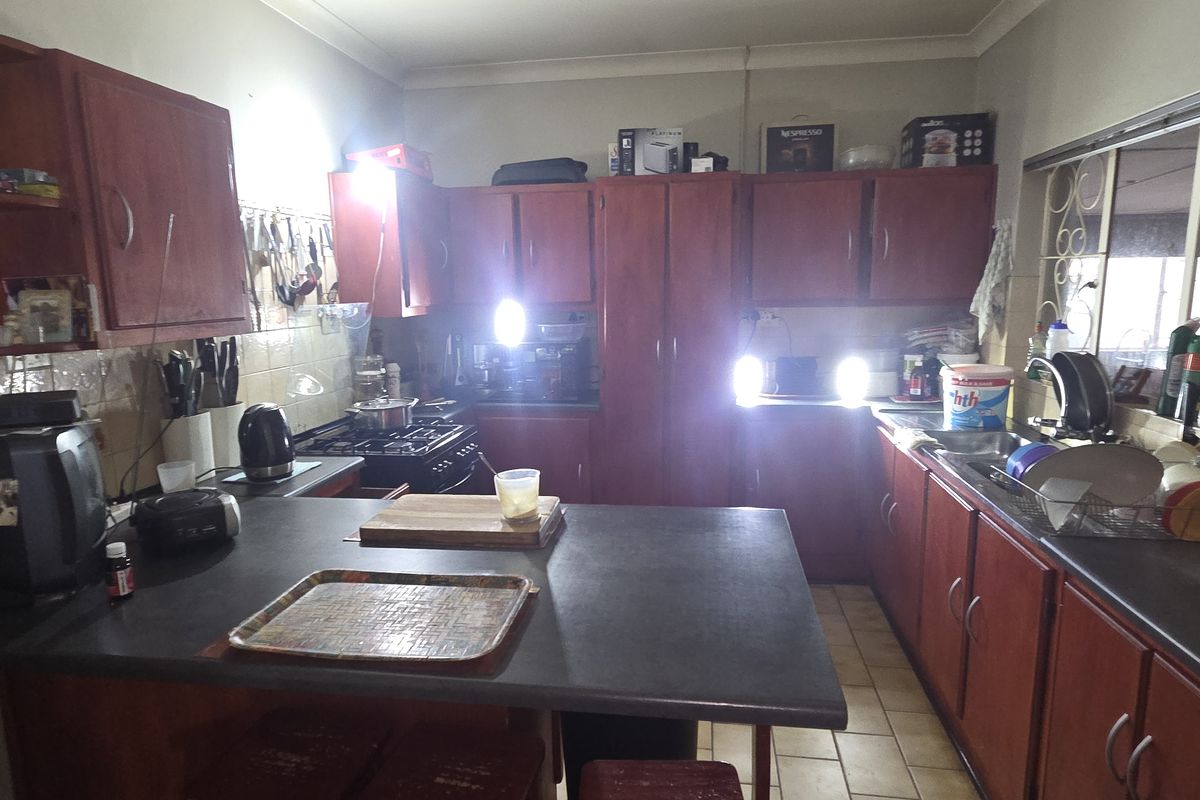 A dated kitchen featuring wooden cabinetry, laminate countertops, a gas hob, and a double sink, with tiled flooring and security bars on the windows.