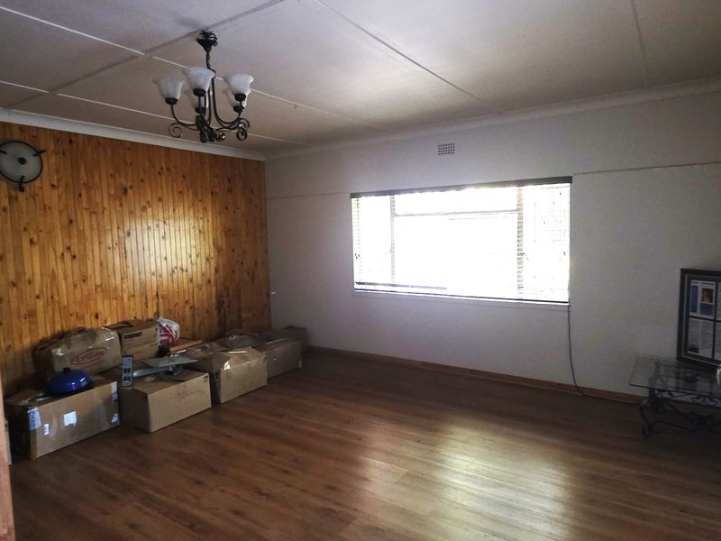 Spacious living room featuring wood paneling, laminate flooring, and a ceiling light fixture, offering a blank canvas for renovation.