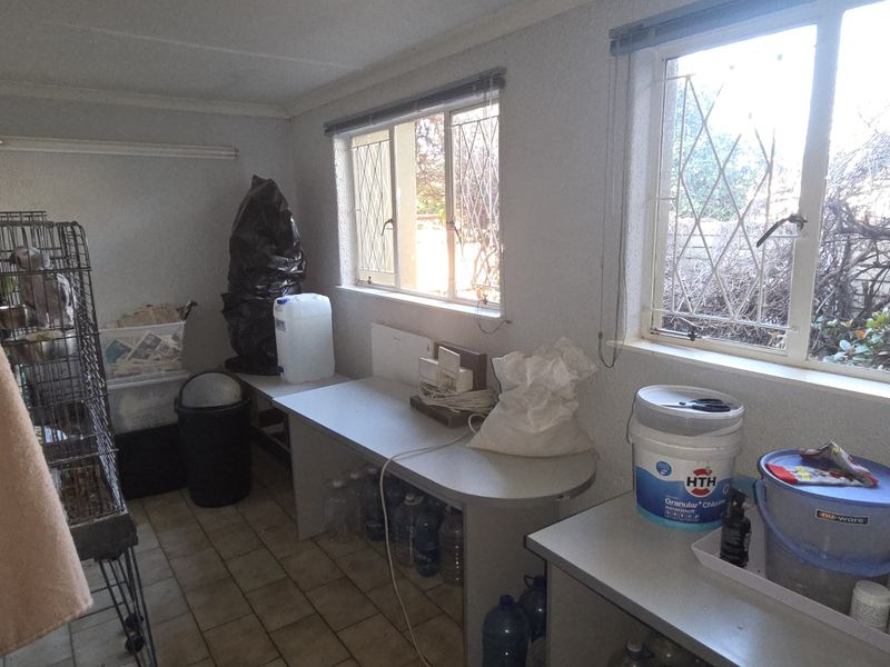 A functional utility space featuring tiled flooring, built-in work surfaces, and windows with security bars, suitable for storage or laundry use.