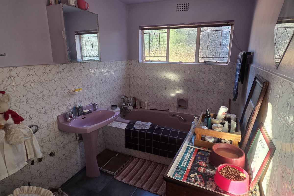 A dated bathroom featuring a pink pedestal basin and matching bathtub with tiled wall finishes and security bars on the window.