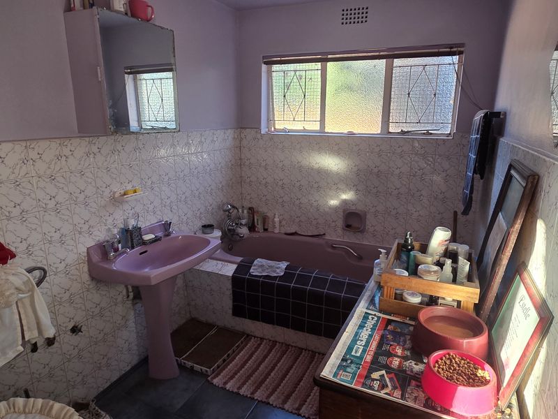 A dated bathroom featuring a pink pedestal basin and matching bathtub with tiled wall finishes and security bars on the window.