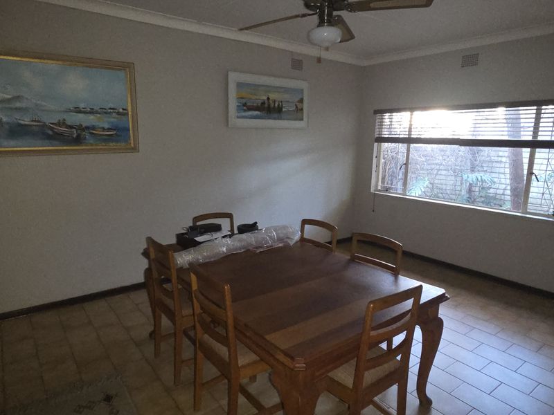 A functional dining room featuring tiled flooring, a ceiling fan, and large windows with venetian blinds, offering a neutral space for family meals.