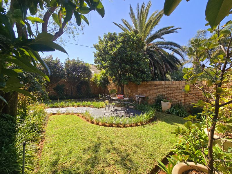 A well-maintained private garden featuring a paved patio area, lush lawn, and established perimeter brick walling.