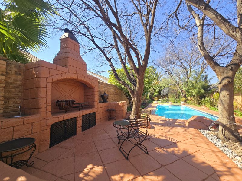 Outdoor entertainment area featuring a built-in brick braai, paved patio space, and a swimming pool set within a landscaped garden.