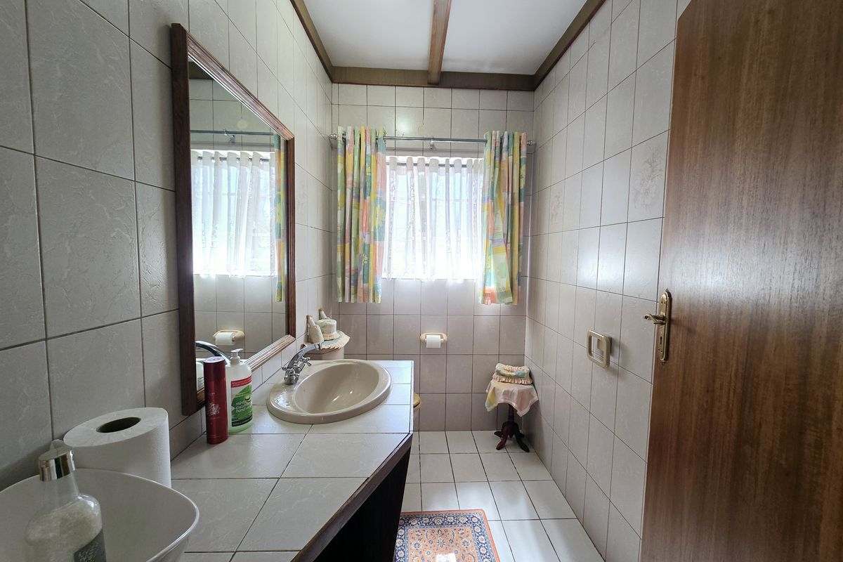 A functional bathroom featuring tiled walls and flooring, a vanity basin with a tiled countertop, and a wall-mounted mirror.