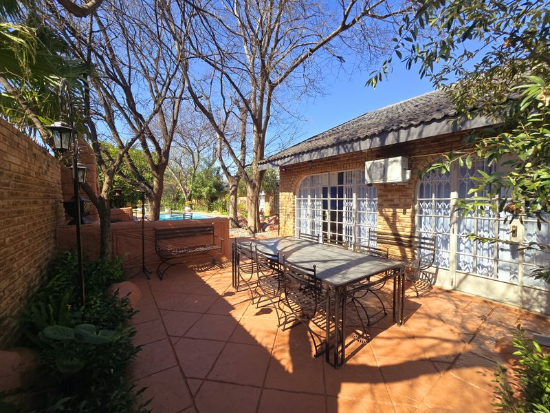 A paved outdoor patio area featuring brick walls, security gates, and an integrated air conditioning unit, overlooking a garden and pool area.