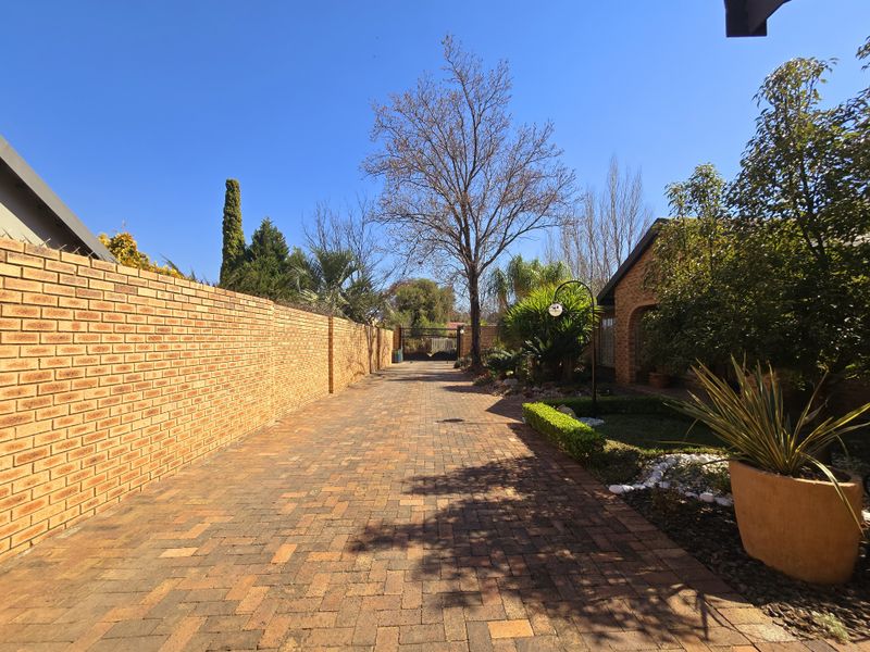 A well-maintained front driveway featuring brick paving, a high brick boundary wall, and established garden landscaping leading toward the property entrance.