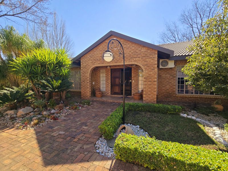 A well-maintained brick front facade featuring an arched entrance, paved walkway, and established garden landscaping.