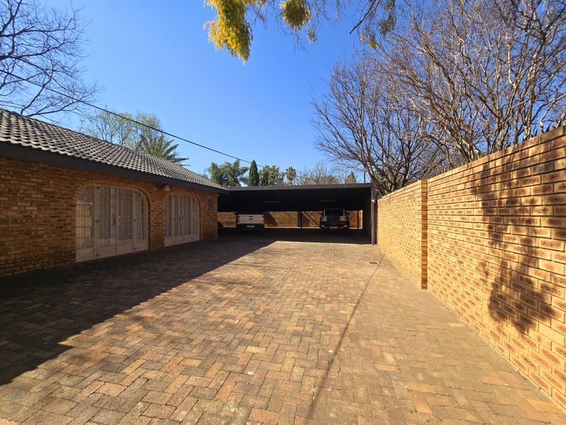 A spacious paved driveway leading to a covered carport area, featuring brick boundary walls and a classic tiled roof facade.