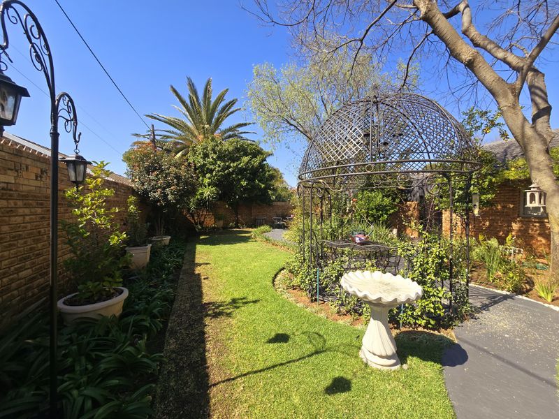 A well-maintained garden featuring a lawn, paved pathways, brick boundary walls, and a decorative wrought iron gazebo.
