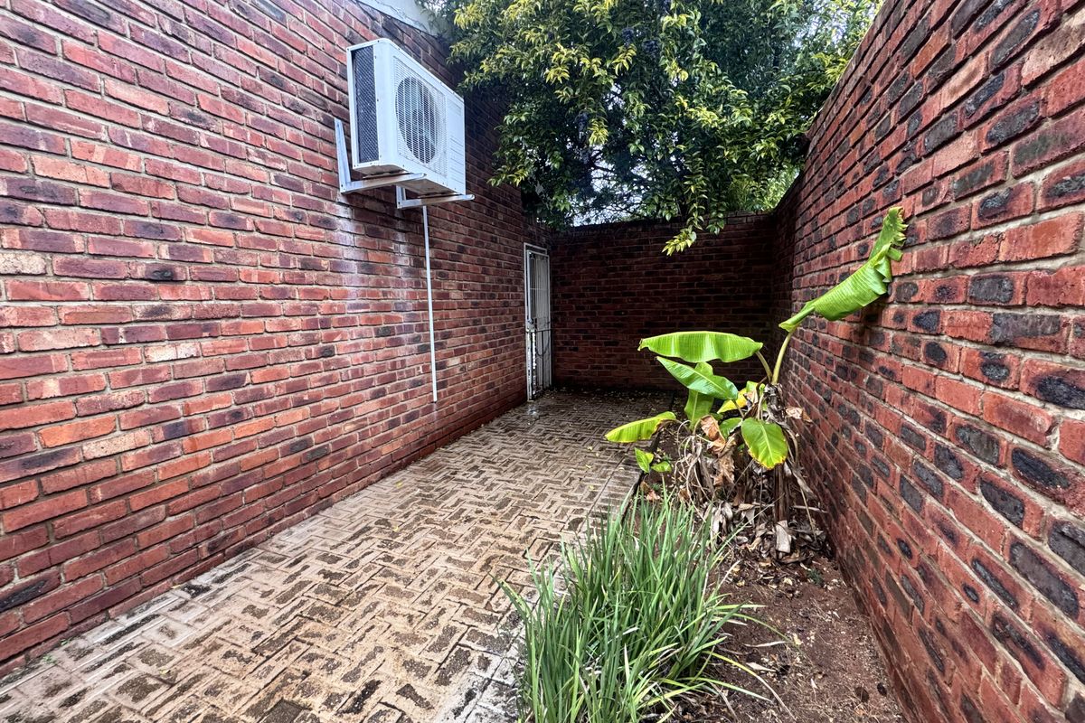 A narrow rear exterior passage featuring exposed brick walls, paved flooring, and a wall-mounted air conditioning unit.