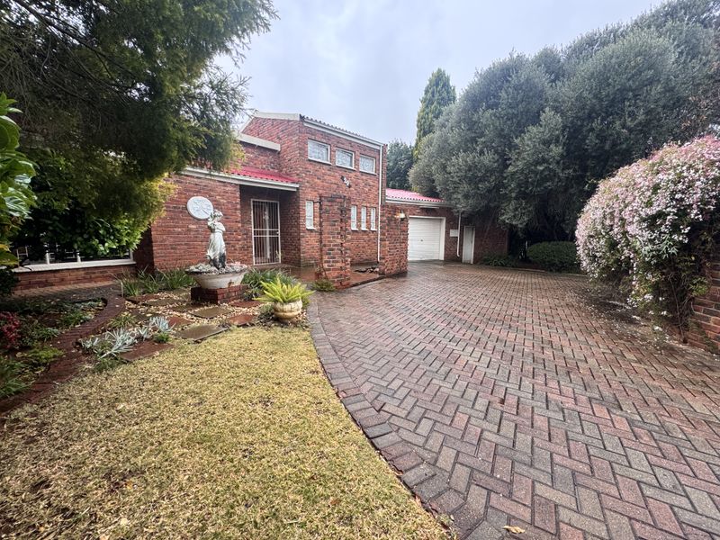 Front view of a brick house featuring a paved driveway, integrated garage, and established garden surroundings.