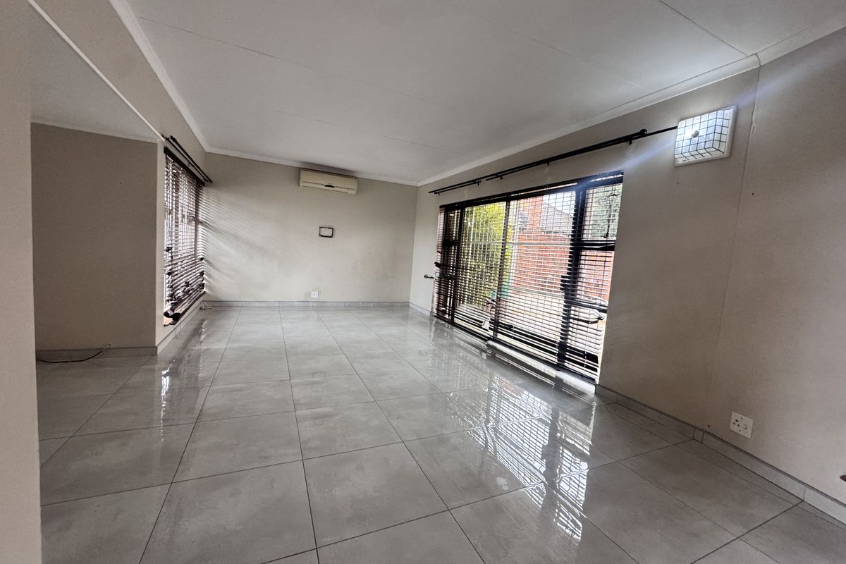 A spacious, empty living room featuring large format floor tiles, a wall-mounted air conditioning unit, and sliding glass doors leading to the exterior.
