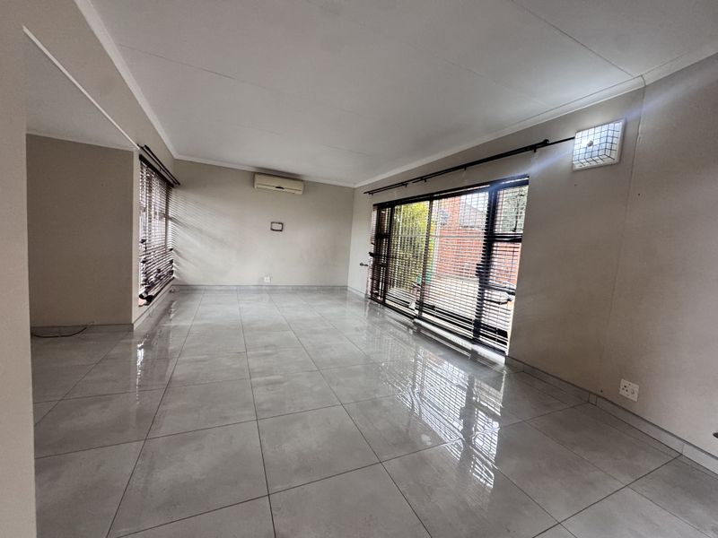 A spacious, empty living room featuring large format floor tiles, a wall-mounted air conditioning unit, and sliding glass doors leading to the exterior.
