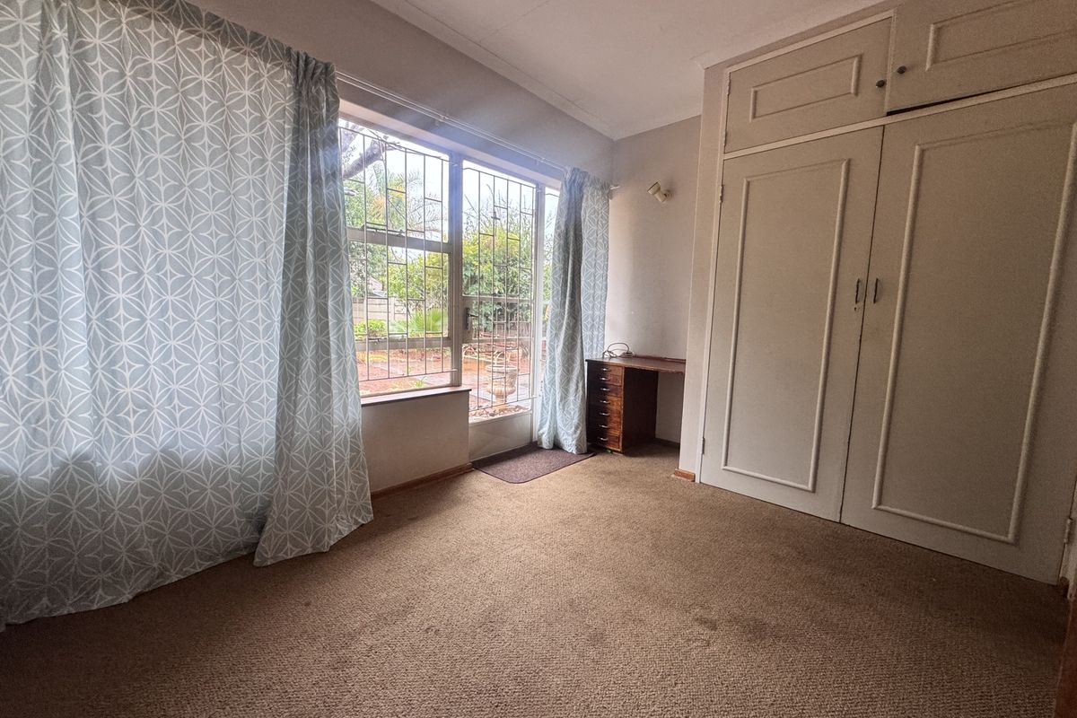 A bedroom featuring built-in cupboards, security bars on the windows, and carpeted flooring, offering a functional space with natural light.