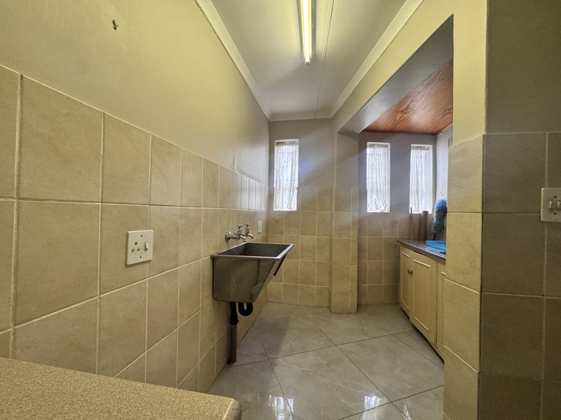A functional laundry room featuring a stainless steel utility sink, tiled walls, and built-in cabinetry with ample floor space.